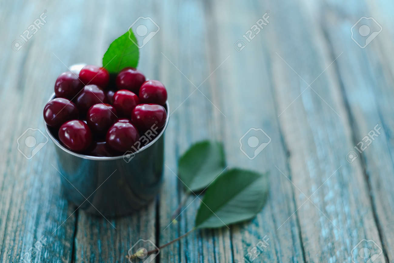 Cherries in a steel mug on a wooden background. - 154903168 Cherries in a steel mug on a wooden background. - 154903168