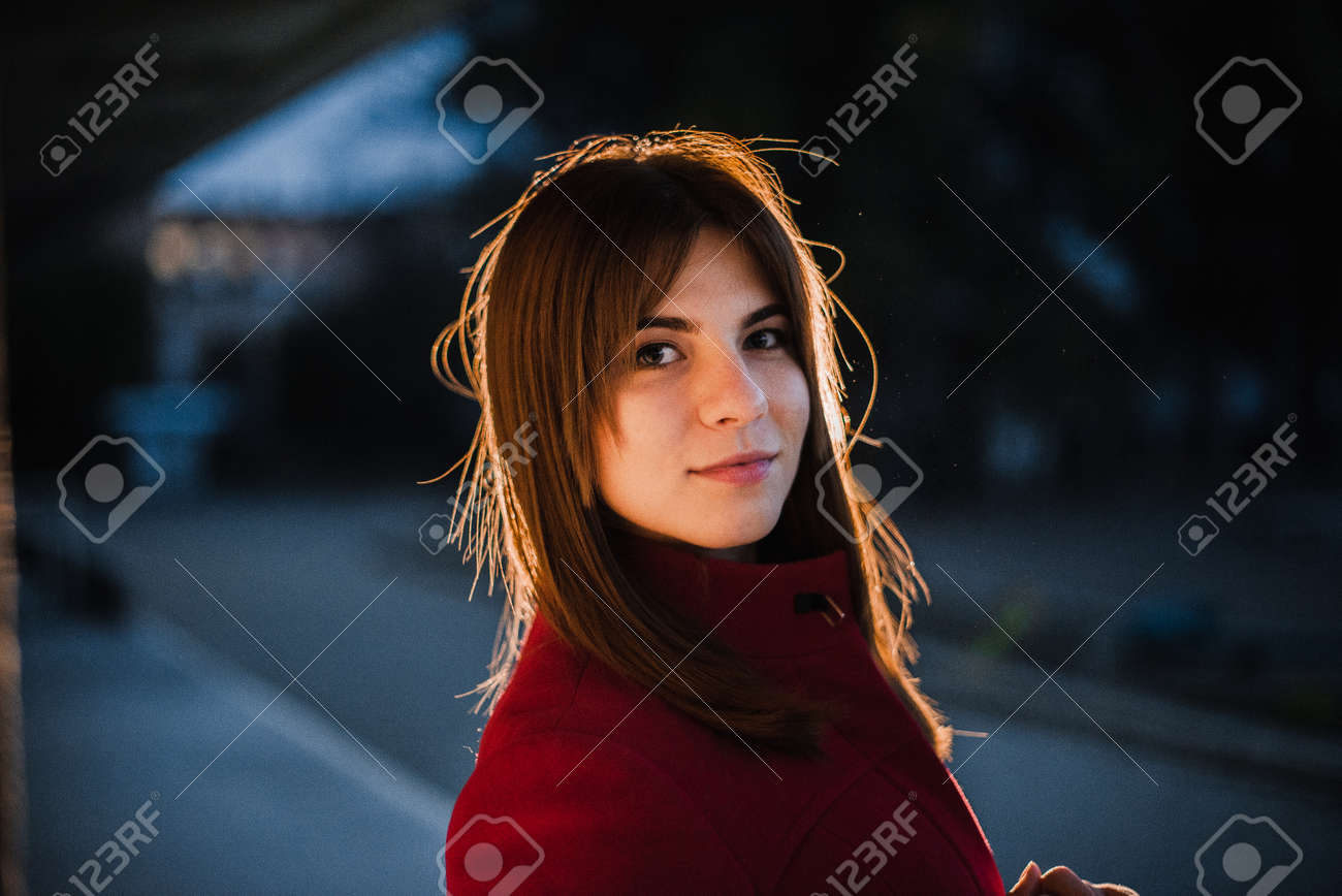 Young beautiful girl in a red coat and hat in the evening in the city. - 155052716 Young beautiful girl in a red coat and hat in the evening in the city. - 155052716