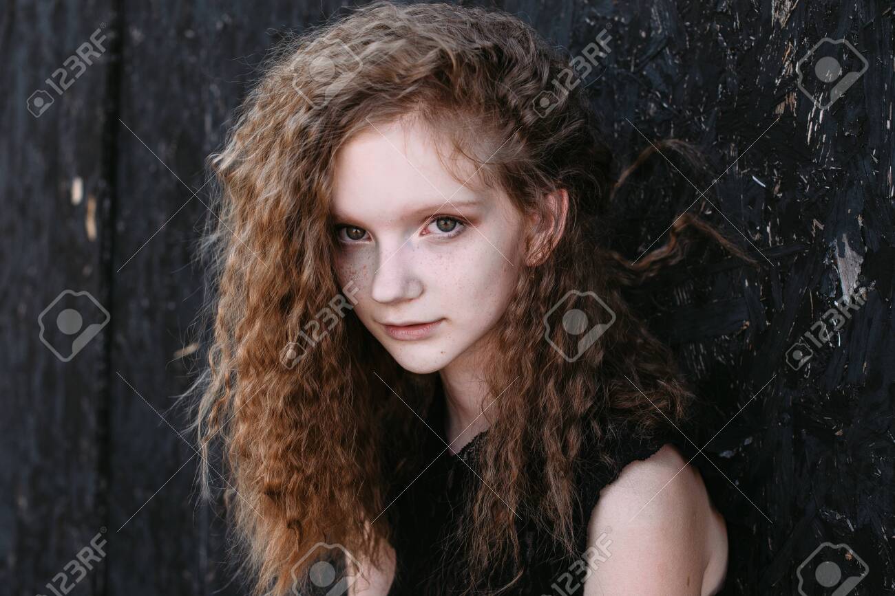 Red-haired girl in a black dress near a dark textured wall. - 155052753 Red-haired girl in a black dress near a dark textured wall. - 155052753