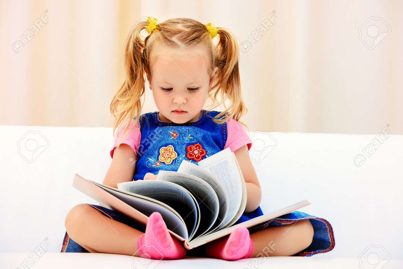 可愛い少女はソファの上に座っていると 子供用絵本を見てします 幸せな子供時代 の写真素材 画像素材 Image