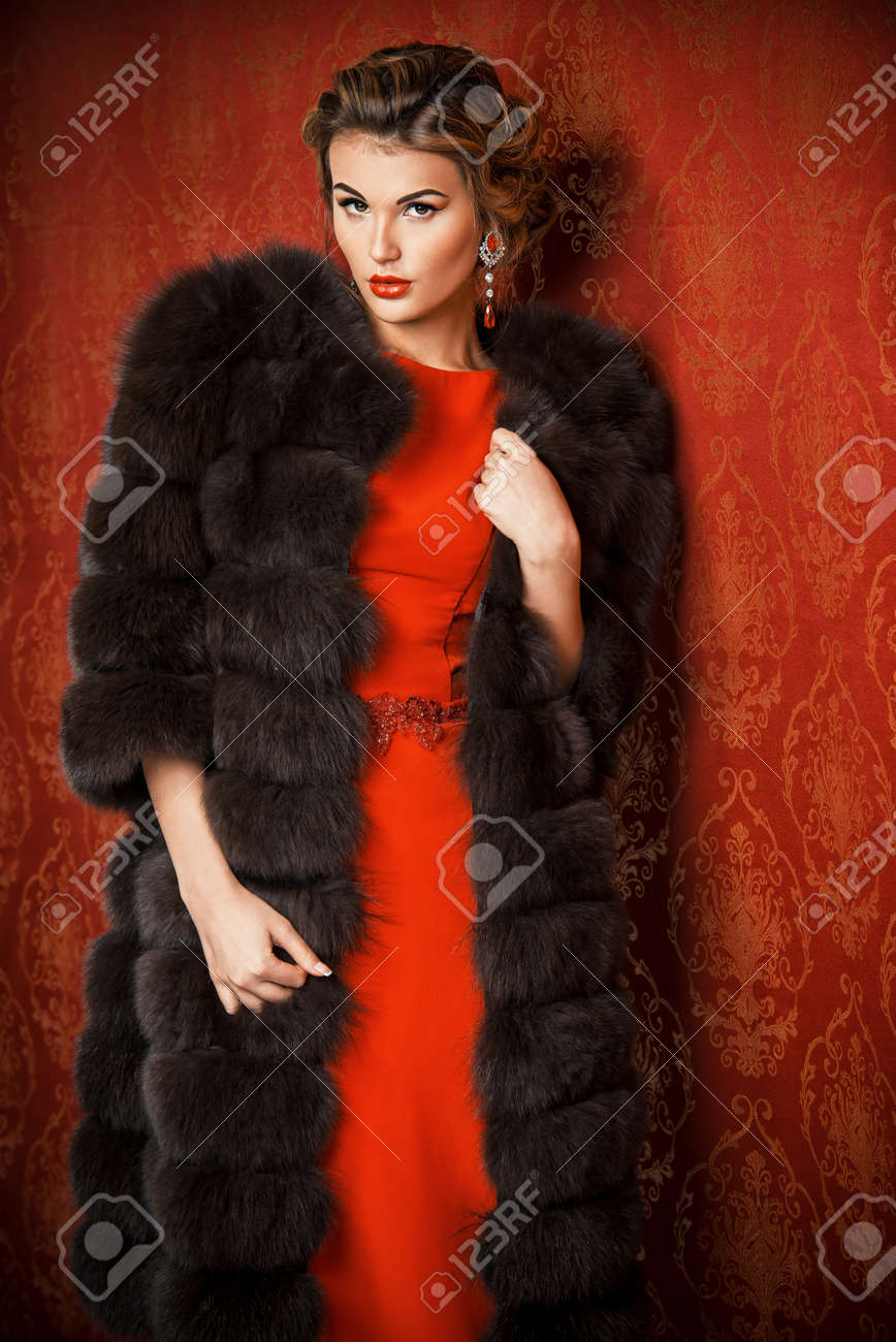 赤いドレスとビンテージ壁紙によって魅力的な豪華な毛皮のコートで美しい女性の肖像画 高級 豊かなライフ スタイル ジュエリー ファッションを撮影しました の写真素材 画像素材 Image