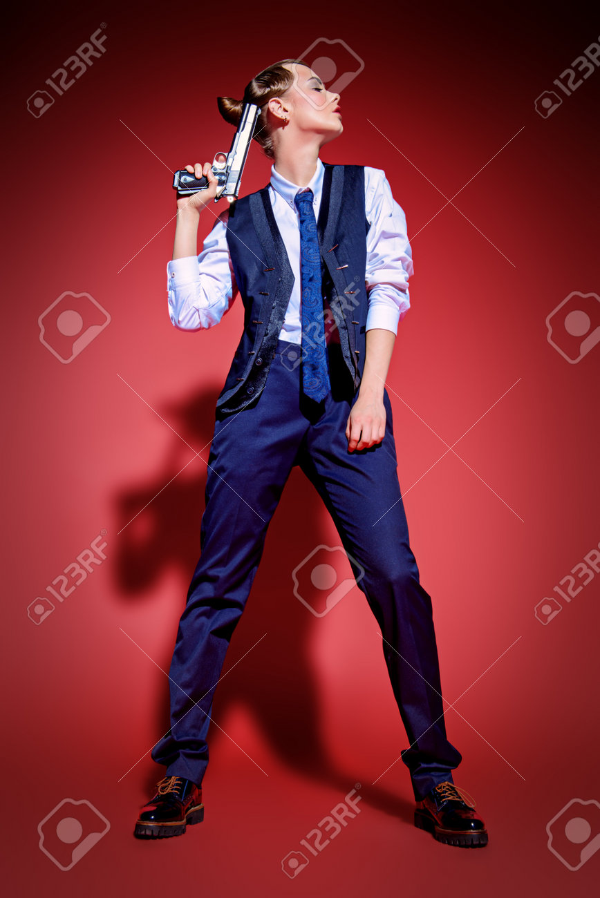 銃を持った男のスーツでポーズ 魅力的な若い女性の肖像画 ギャング スタイル 男のスタイルの服 背景が赤です ファッションを撮影しました の写真素材 画像素材 Image