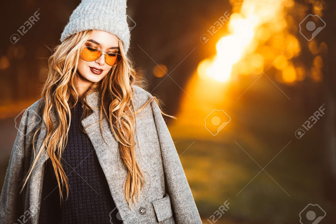 Autumn fashion. Happy young woman wearing warm sweater, a coat and a woolen hat walking in the park at a sunny autumn day. - 92295339 Autumn fashion. Happy young woman wearing warm sweater, a coat and a woolen hat walking in the park at a sunny autumn day. - 92295339