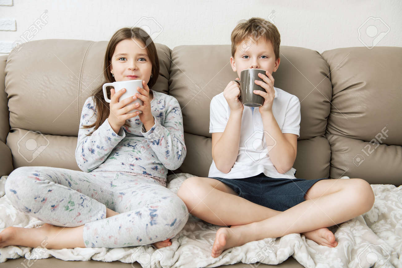 Cute boy and girl are sitting on the couch with cups. Fashion home shot. Childhood. Kid's fashion. - 117767556 Cute boy and girl are sitting on the couch with cups. Fashion home shot. Childhood. Kid's fashion. - 117767556