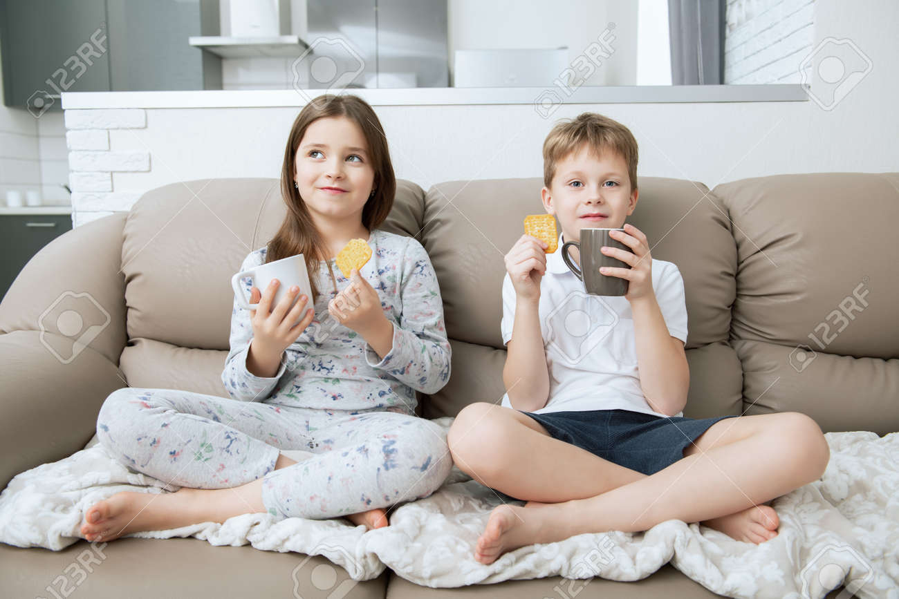 Cute boy and girl are sitting on the couch with cups. Fashion home shot. Childhood. Kid's fashion. - 118168562 Cute boy and girl are sitting on the couch with cups. Fashion home shot. Childhood. Kid's fashion. - 118168562