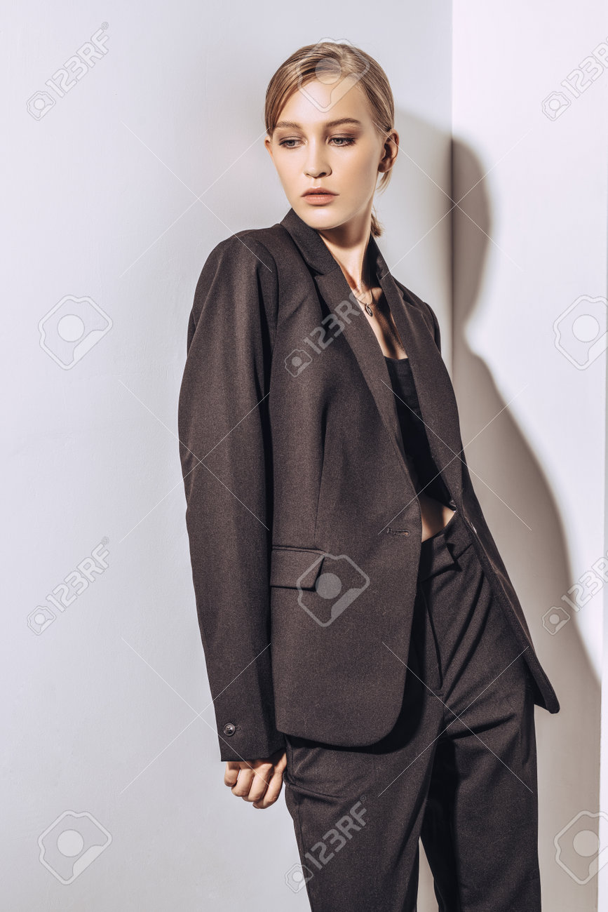 パンツスーツ　接写 白い壁でポーズをとって黒いフォーマルなスーツを着た美しいブロンドの女性の肖像画。ファッションショット。の写真素材・画像素材 Image  160240829