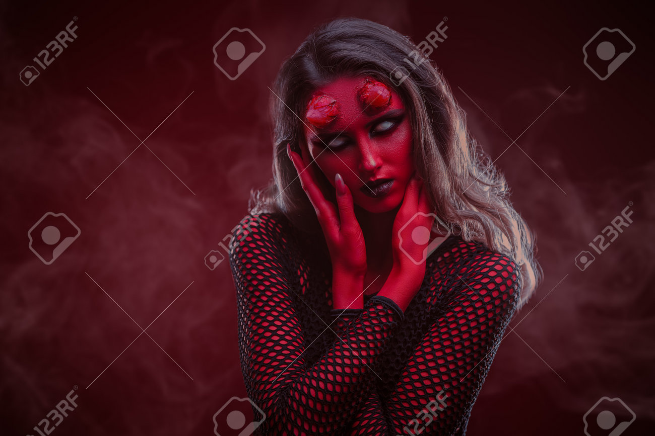 A Scary And Sexy Devil Girl With Bloody Horns And Colorless Eyes On A Dark  Red Studio Background With A Haze. Copy Space. Halloween. Thriller, Horror.  Stock Photo, Picture and Royalty Free, image size:1300x867