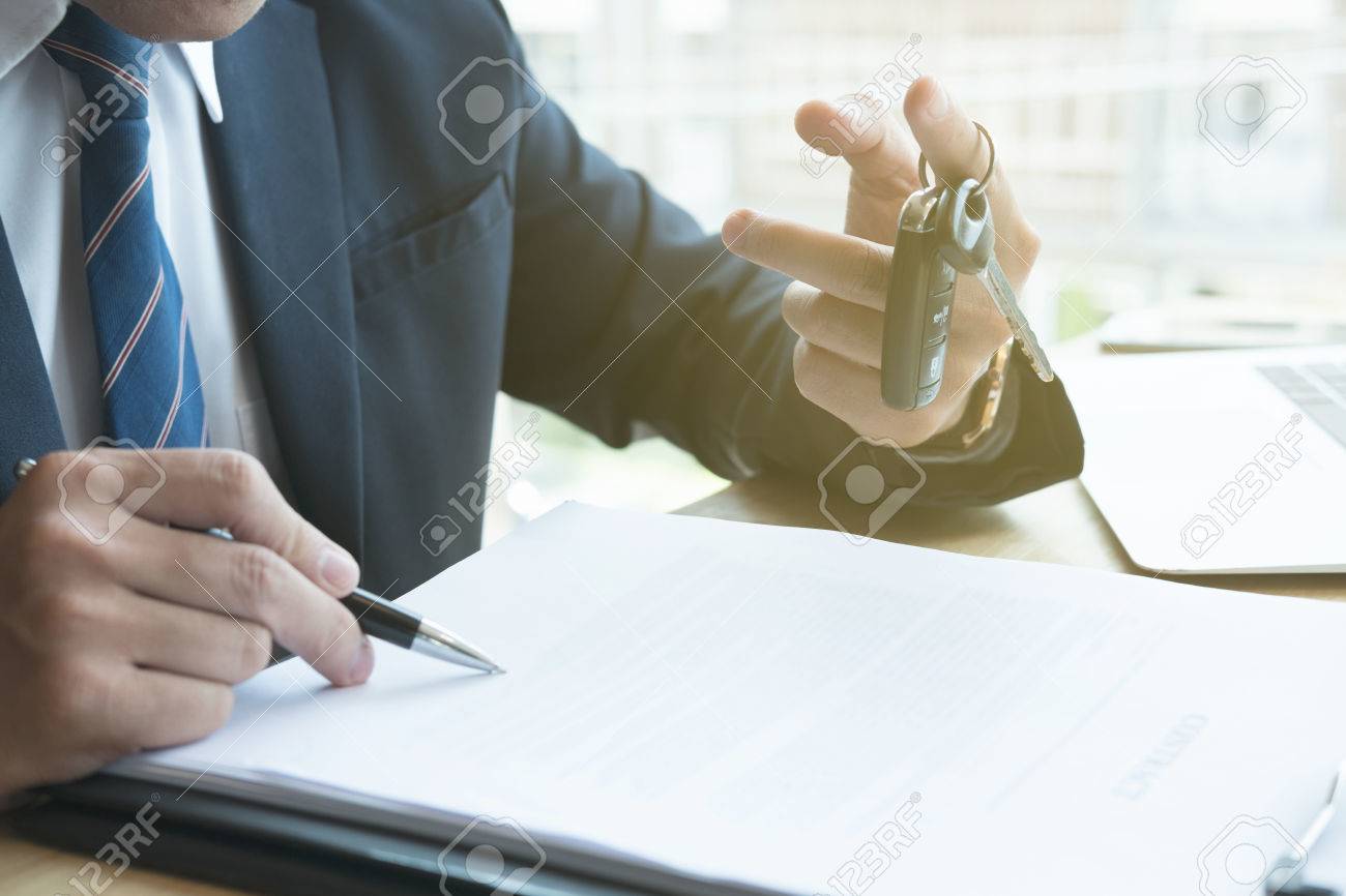 young businessman sign sales contract with car key at office