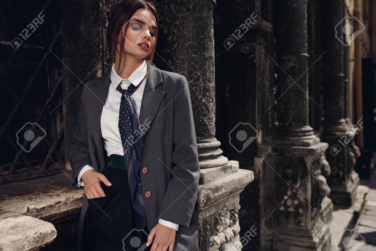 通りに立っているファッション性の高い服でファッショナブルな女性 屋外女性らしいスタイリッシュな服でポーズでセクシーな美女 エレガントなオーバー コート シャツ スカート ネクタイ秋に女性モデルのポートレート の写真素材 画像素材 Image