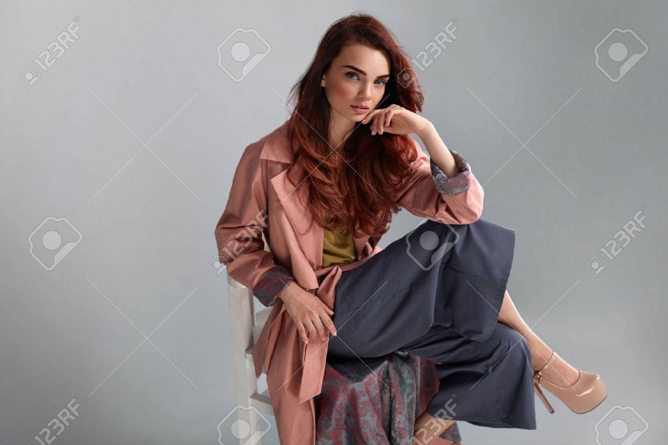 ファッション モデル スタイル スタジオの灰色の背景にポーズのスタイリッシュな服でファッショナブルな女性 美しいセクシーな女の子が椅子に座っているピンクのコート 紫のズボン ベージュの靴を履いています 高分解能 の写真素材 画像素材 Image
