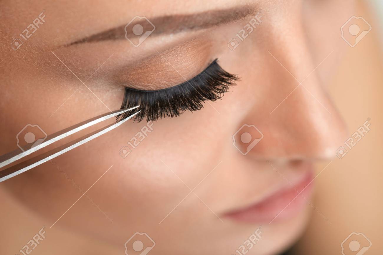 まつげ 美しい女性がピンセットでつけまつげを適用すること プロの顔メイク 滑らかな肌と長い黒太いまつげと若い女性モデルの顔のクローズ アップ 高分解能 の写真素材 画像素材 Image