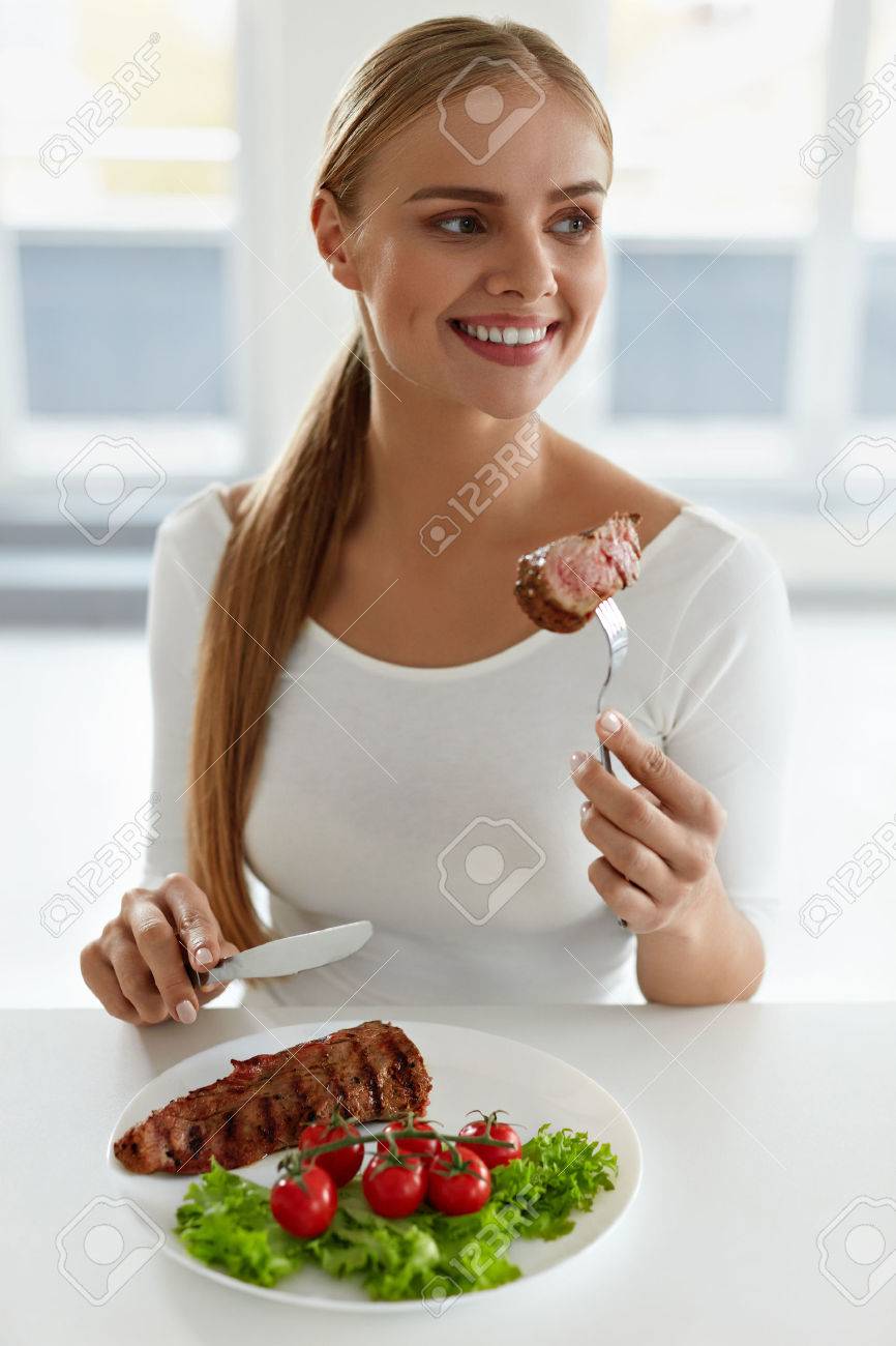 女性の食べる食べ物 美しいディナー キッチンで新鮮な野菜と美味しい焼肉の女性を持つ笑顔します 健康的な魅力的な女の子とトマト 牛肉ステーキを持つダイニング サラダ 栄養 の写真素材 画像素材 Image