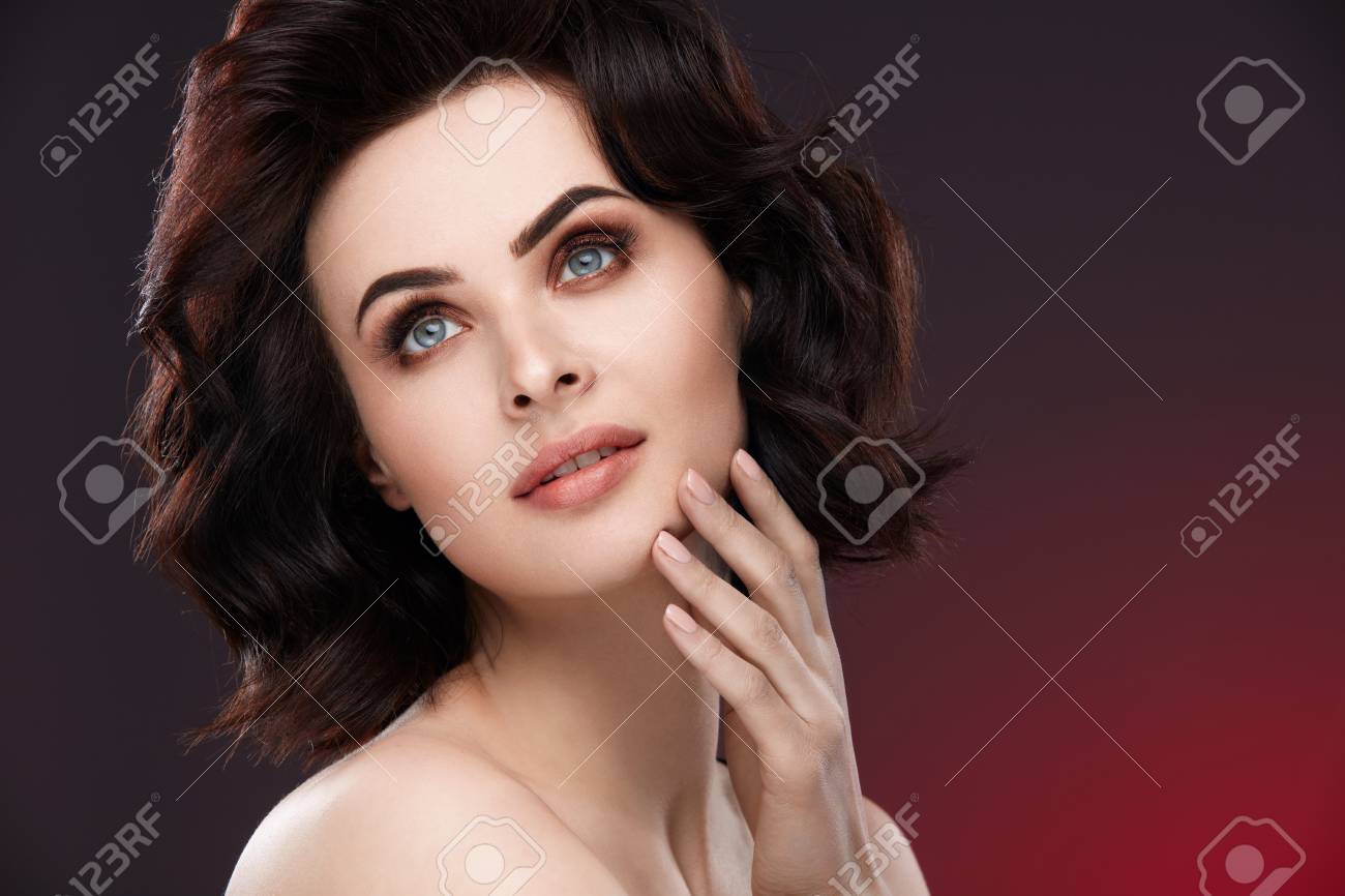 顔のスキンケア 化粧と赤の背景に健康な新鮮な顔の皮膚に触れる華やかな髪型と美しい女性の肖像画 高分解能 の写真素材 画像素材 Image