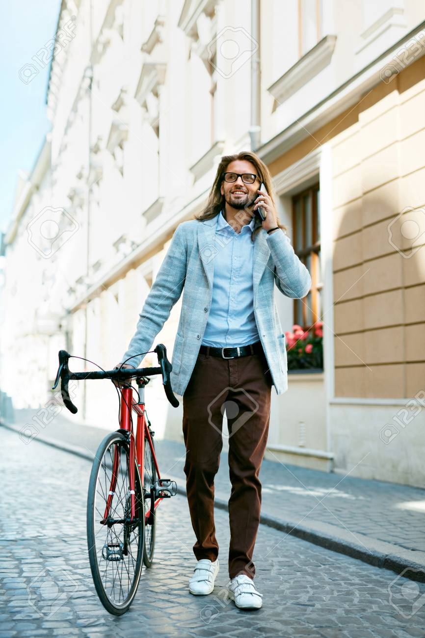 路上を歩いている間に自転車を持つ男が電話で呼び出す 市街地でモダンな赤い自転車とスタイリッシュなカジュアルな服を着た自信のある若い男性の肖像画 高品質の画像 の写真素材 画像素材 Image