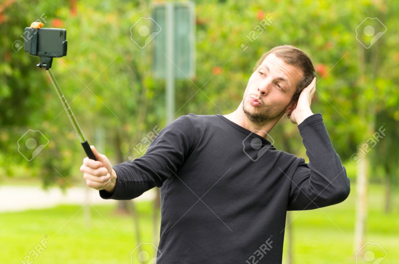 ヒスパニック系男性左の腕を使用して彼の頭をなでる公園環境で Selfie 棒でポーズします の写真素材 画像素材 Image