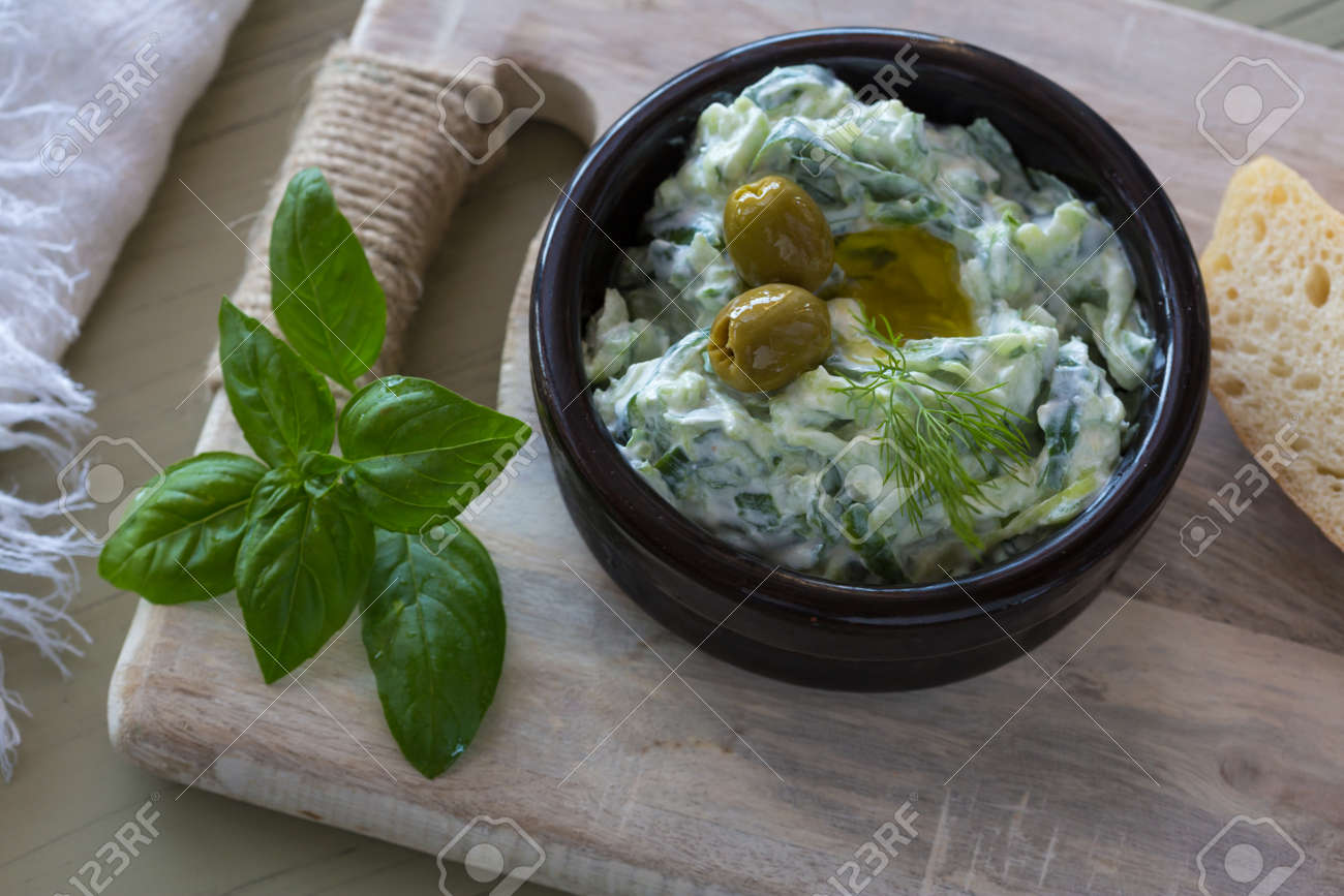 Greek dip sauce or dressing tzatziki and ingredients decorated with olive oil and basil on wooden table. - 150727569 Greek dip sauce or dressing tzatziki and ingredients decorated with olive oil and basil on wooden table. - 150727569