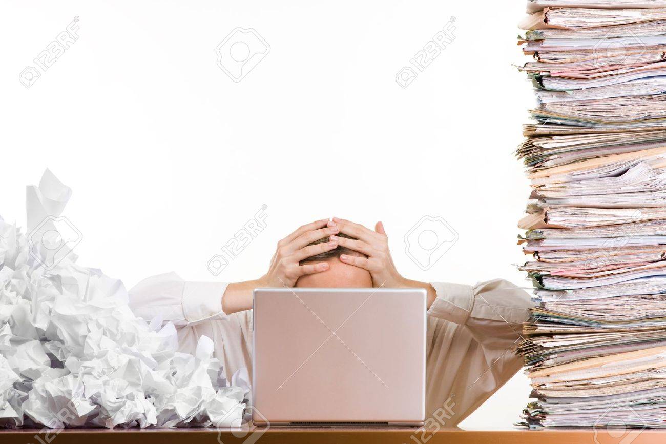 a stressed person holding his head behind a laptop surrounded