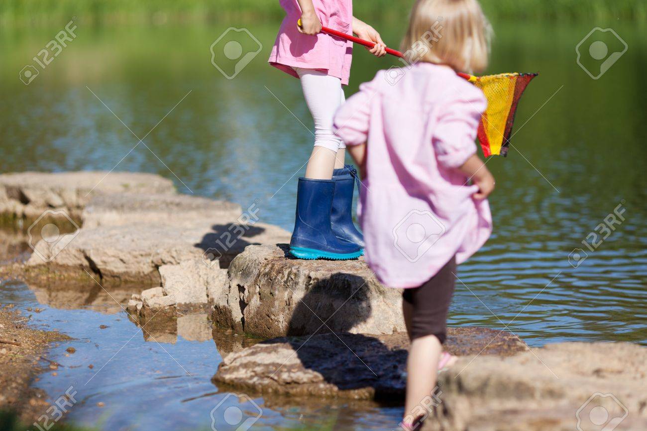 小さい網で釣り長靴の湖の側で 水で遊ぶ二人の少女 の写真素材 画像素材 Image