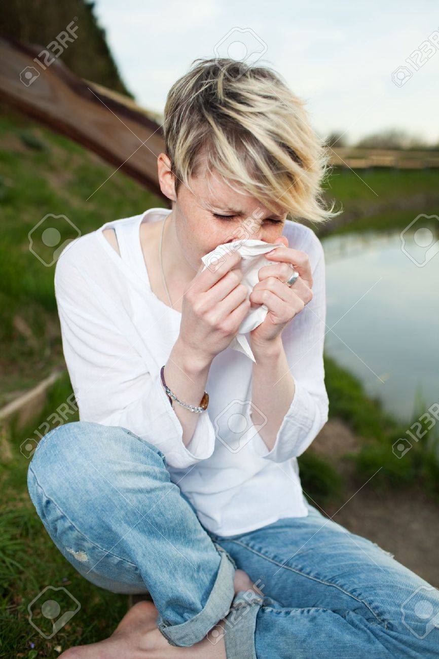 Young woman sneezing into handkerchief by the lake - 21290213 Young woman sneezing into handkerchief by the lake - 21290213