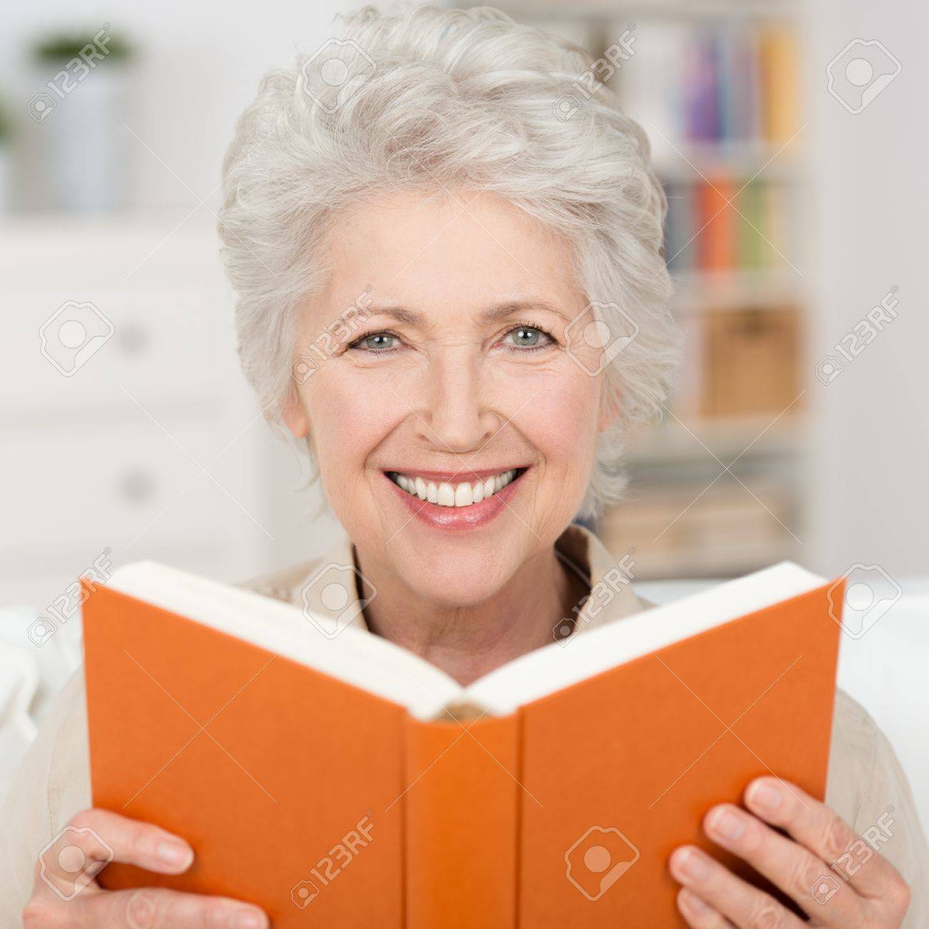 家でのんびり素敵な笑顔と魅力的な灰色髪年配の女性が本を読んでください の写真素材 画像素材 Image