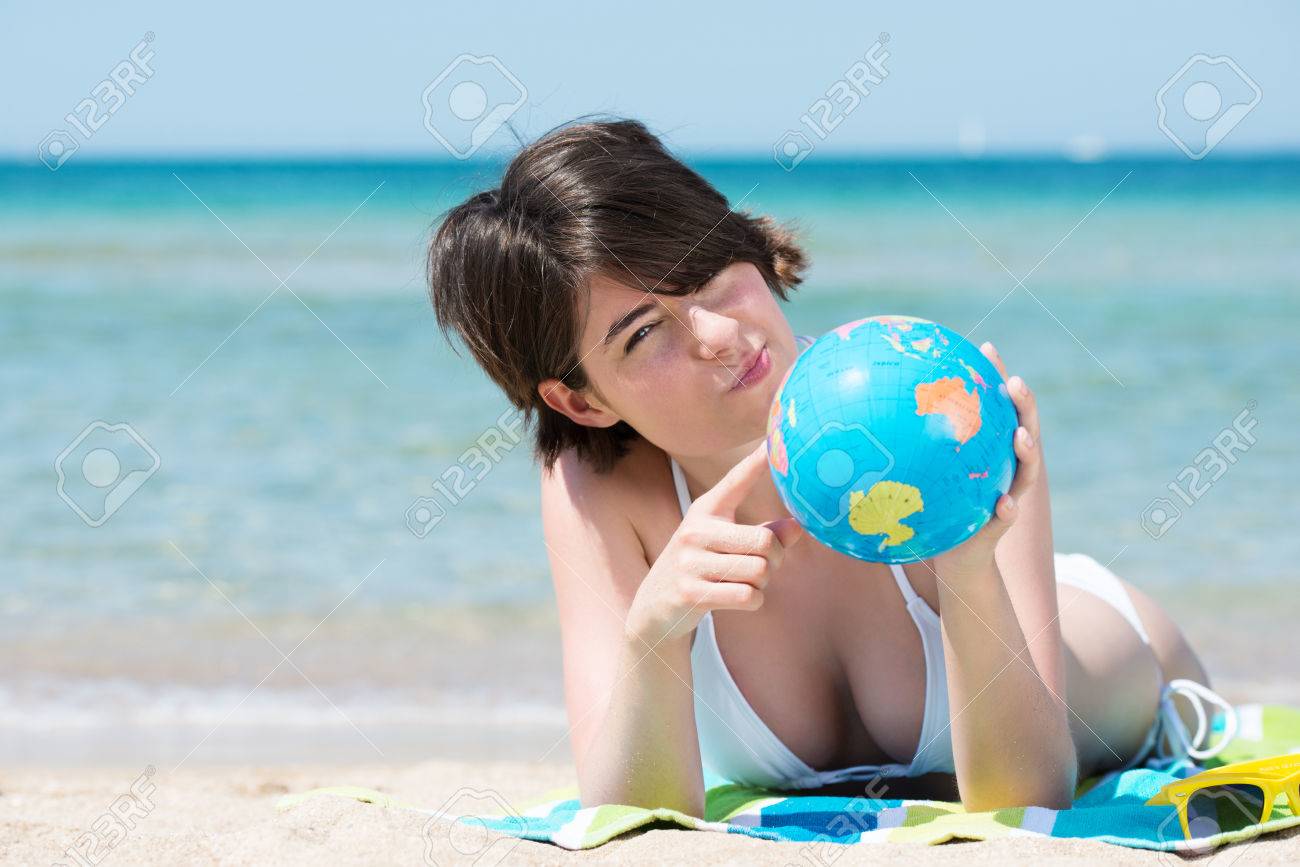 思いやりのある若い女性彼女の手と空気を見つめながら気まぐれな表現で世界中で日当たりの良い熱帯のビーチのタオルの上に横たわって夏休みを決定します の写真素材 画像素材 Image