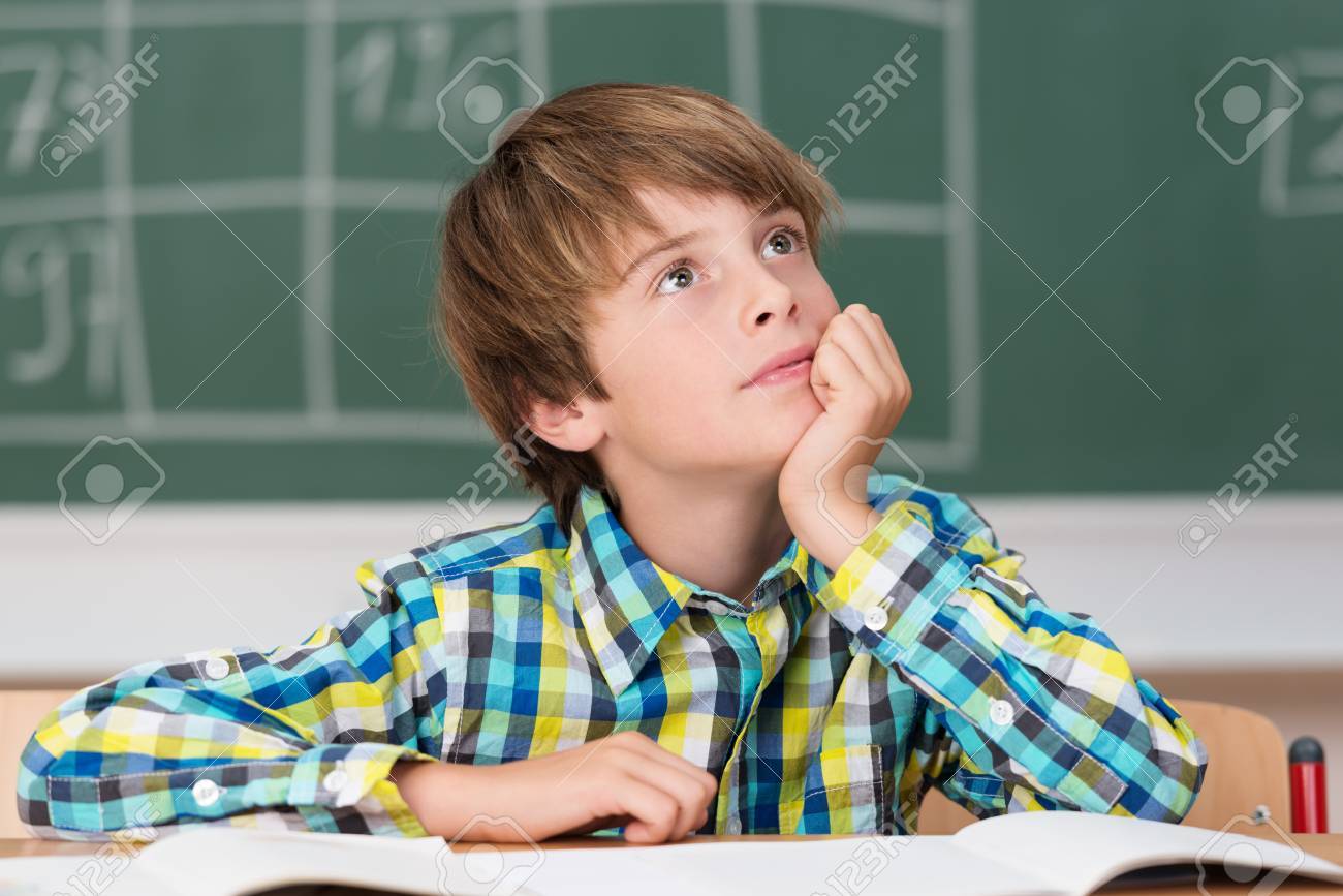 young schoolboy daydreaming in class as he sits at his desk in daydreaming in class