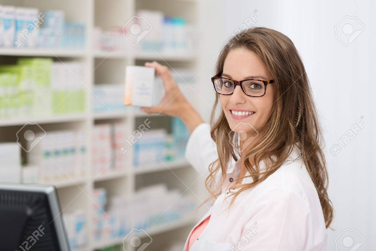 Smiling attractive young female pharmacist promoting a product in a blank white box she is holding up in her hand in the pharmacy - 34559856 Smiling attractive young female pharmacist promoting a product in a blank white box she is holding up in her hand in the pharmacy - 34559856