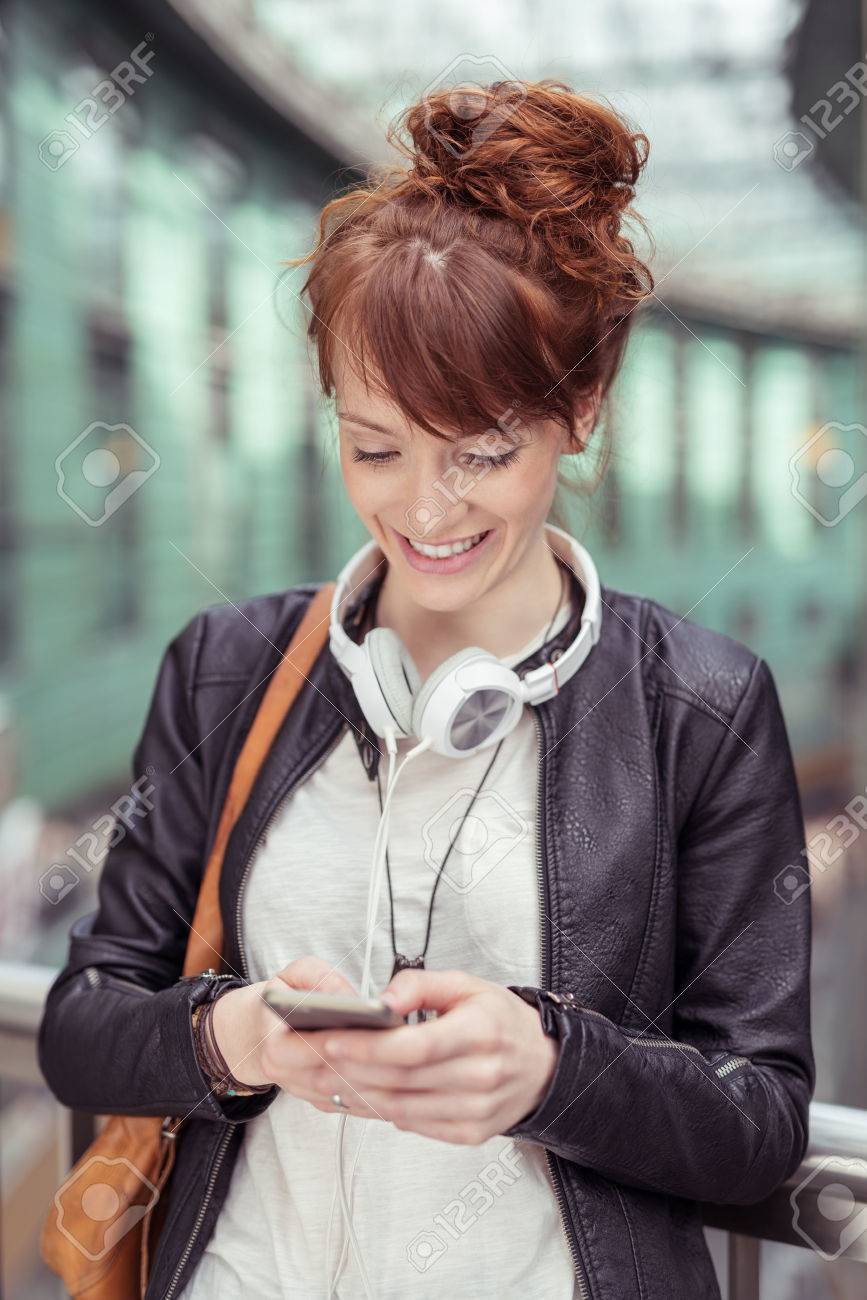 彼女の首と彼女の携帯電話しながら傾いてに対して 手すりと多忙を極めてショルダー バッグ レザー ジャケット ヘッドフォン周りで幸せな若い女を閉じます の写真素材 画像素材 Image