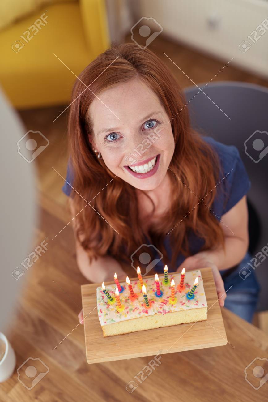 Vivacious Jolie Jeune Femme Rousse Tenant Son Gateau D Anniversaire Avec Des Bougies Allumees Comme Elle Regarde La Camera Avec Un Sourire Rayonnant Banque D Images Et Photos Libres De Droits Image