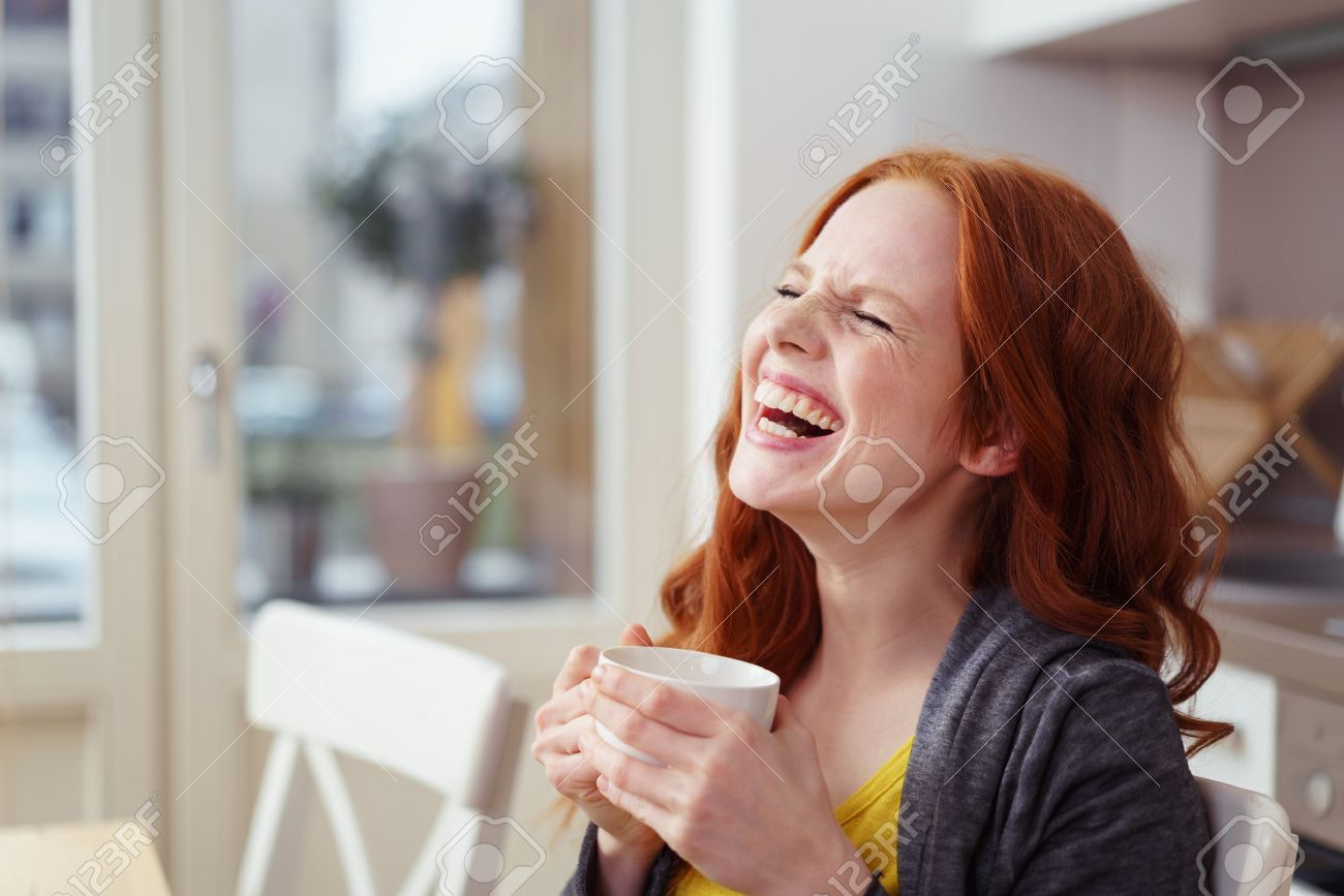 Spontaneous attractive young redhead woman enjoying a good laugh over a morning cup of coffee at home in the apartment - 54149205 Spontaneous attractive young redhead woman enjoying a good laugh over a morning cup of coffee at home in the apartment - 54149205