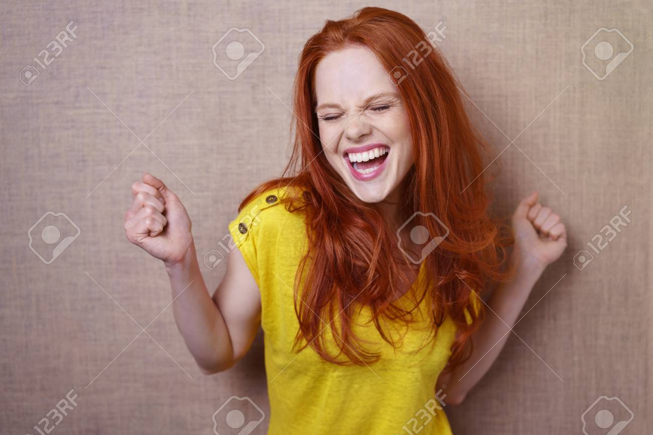 Single gorgeous young red haired woman in yellow shirt dancing or rejoicing about something over simple brown cloth background with copy space - 63935682 Single gorgeous young red haired woman in yellow shirt dancing or rejoicing about something over simple brown cloth background with copy space - 63935682