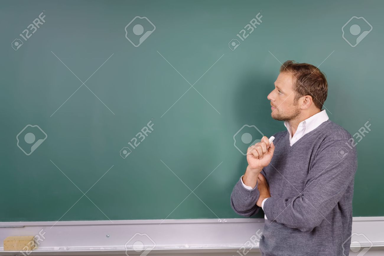 Thoughtful male teacher looking at a blank empty green blackboard with a stick of chalk in his hand and copy space for your text - 62901998 Thoughtful male teacher looking at a blank empty green blackboard with a stick of chalk in his hand and copy space for your text - 62901998
