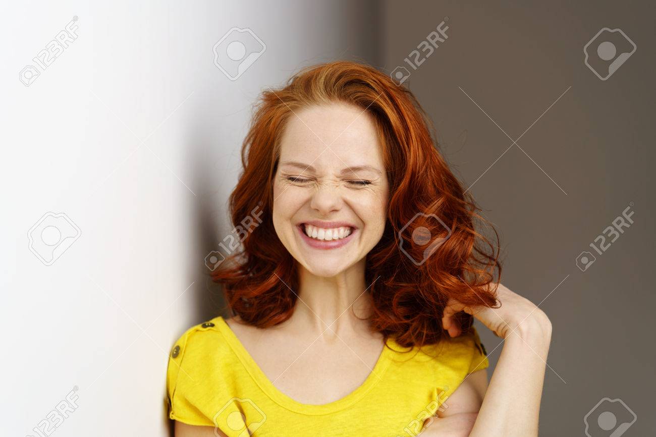 Excited young woman pulling a goofy face with a broad smile as she plays with her shoulder length red hair - 74155672 Excited young woman pulling a goofy face with a broad smile as she plays with her shoulder length red hair - 74155672