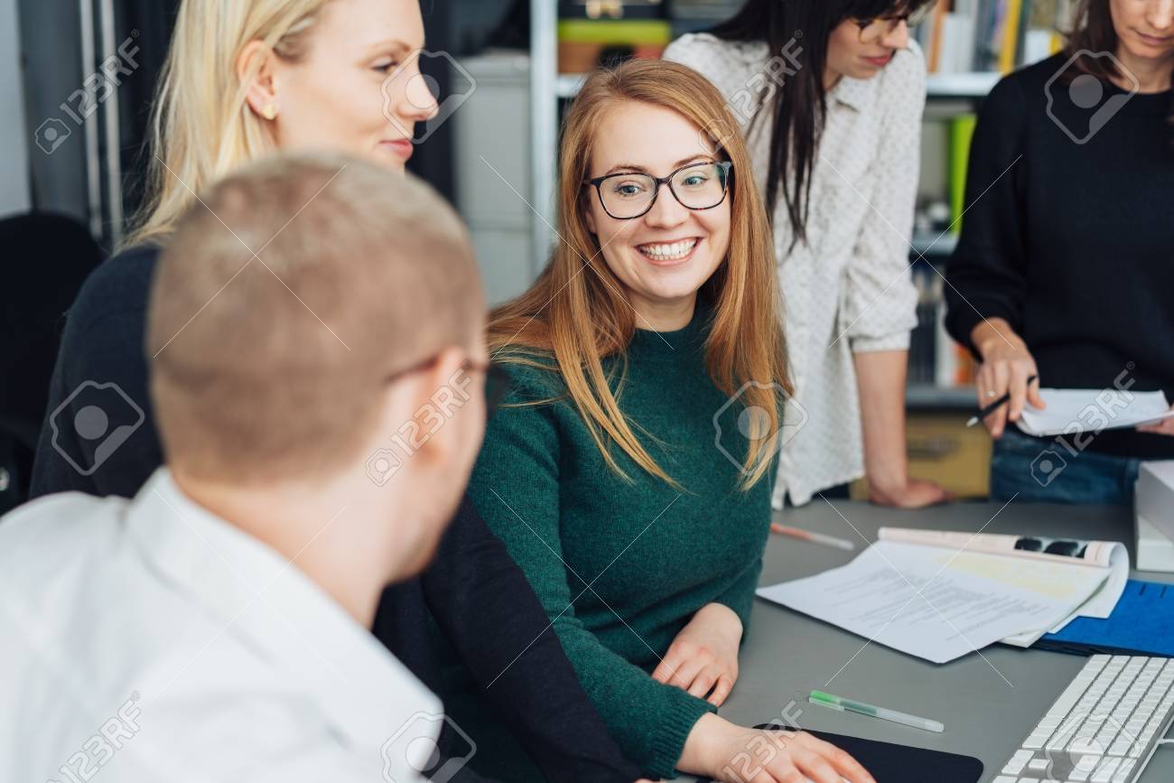 Attractive smiling young businesswoman wearing glasses chatting to a male colleague in a meeting with a pleased smile - 115810121 Attractive smiling young businesswoman wearing glasses chatting to a male colleague in a meeting with a pleased smile - 115810121