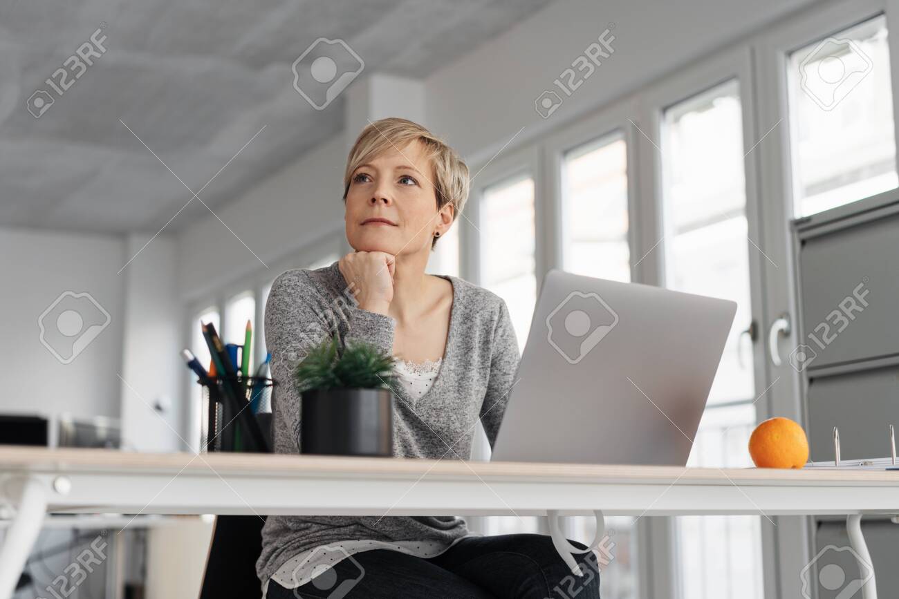 Thoughtful mature blonde woman sitting in front of computer at office - 153539274 Thoughtful mature blonde woman sitting in front of computer at office - 153539274