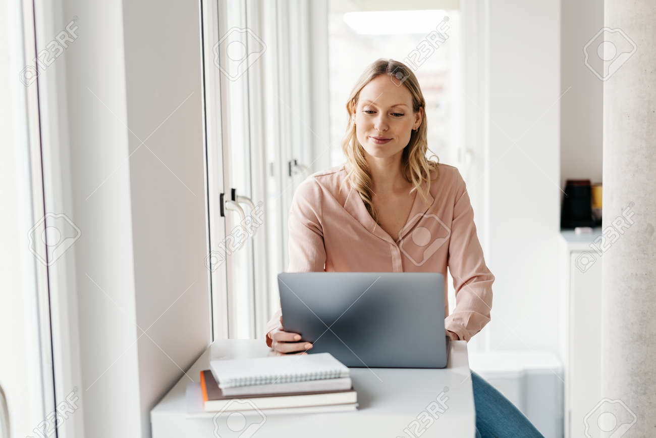 Happy young businesswoman working from home or telecommuting during the lockdown for te Covid-19 pandemic in a high key apartment with copyspace - 167565776 Happy young businesswoman working from home or telecommuting during the lockdown for te Covid-19 pandemic in a high key apartment with copyspace - 167565776