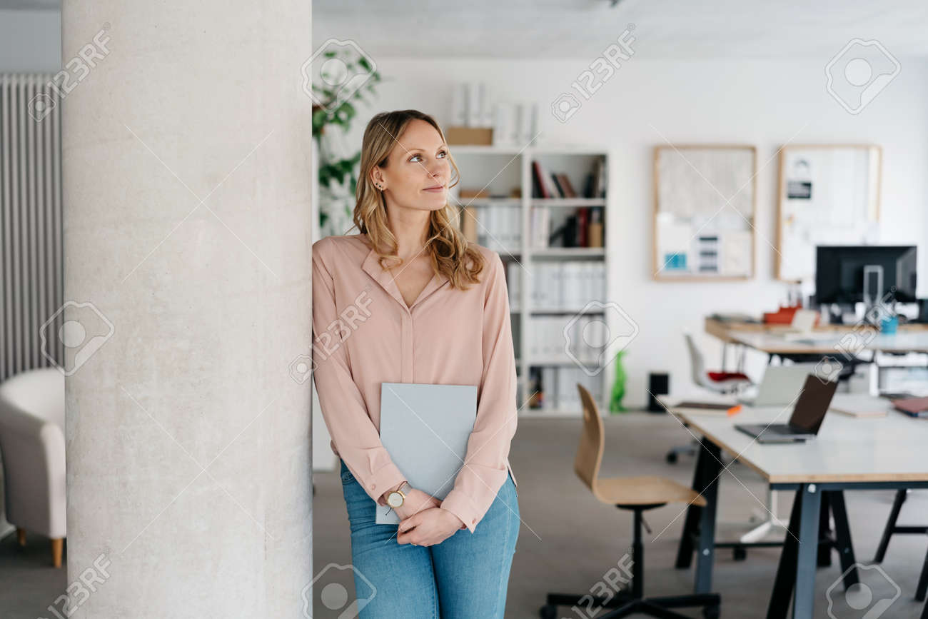 Thoughtful young businesswoman standing daydreaming leaning against an internal office pillar looking up with a quiet smile in a concept of memories, inspiration or planning - 167565784 Thoughtful young businesswoman standing daydreaming leaning against an internal office pillar looking up with a quiet smile in a concept of memories, inspiration or planning - 167565784