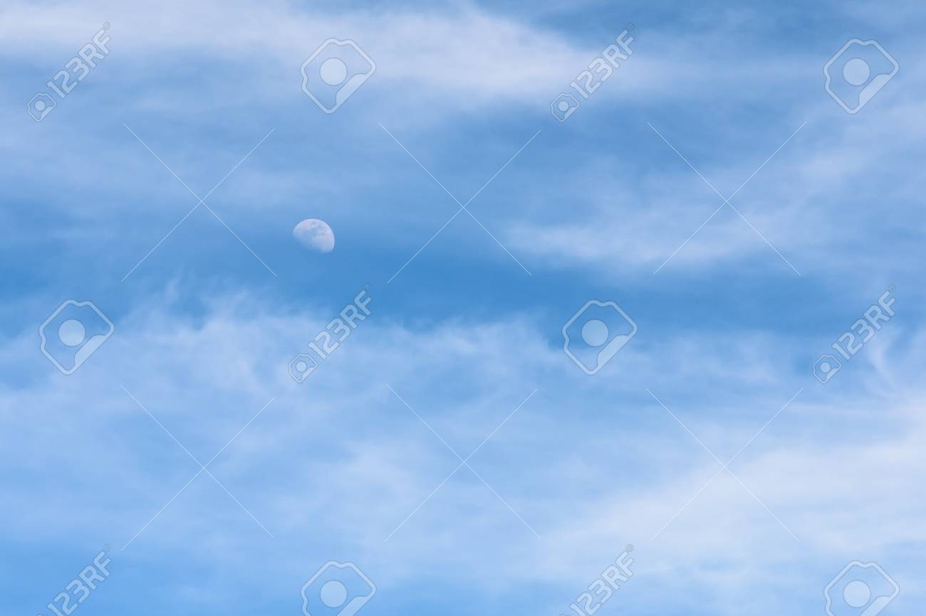 moon visible in daylight blue sky with white soft clouds stock photo