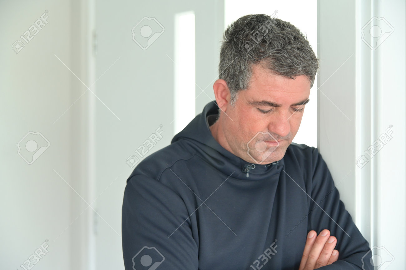 Sad man (male age 40-50) looking down leaning against a home wall. - 168379490 Sad man (male age 40-50) looking down leaning against a home wall. - 168379490