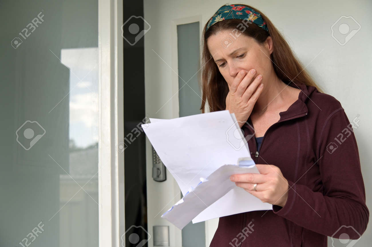 Shocked adult woman (female age 25-35) reading a letter outside a home front door. - 169904524 Shocked adult woman (female age 25-35) reading a letter outside a home front door. - 169904524