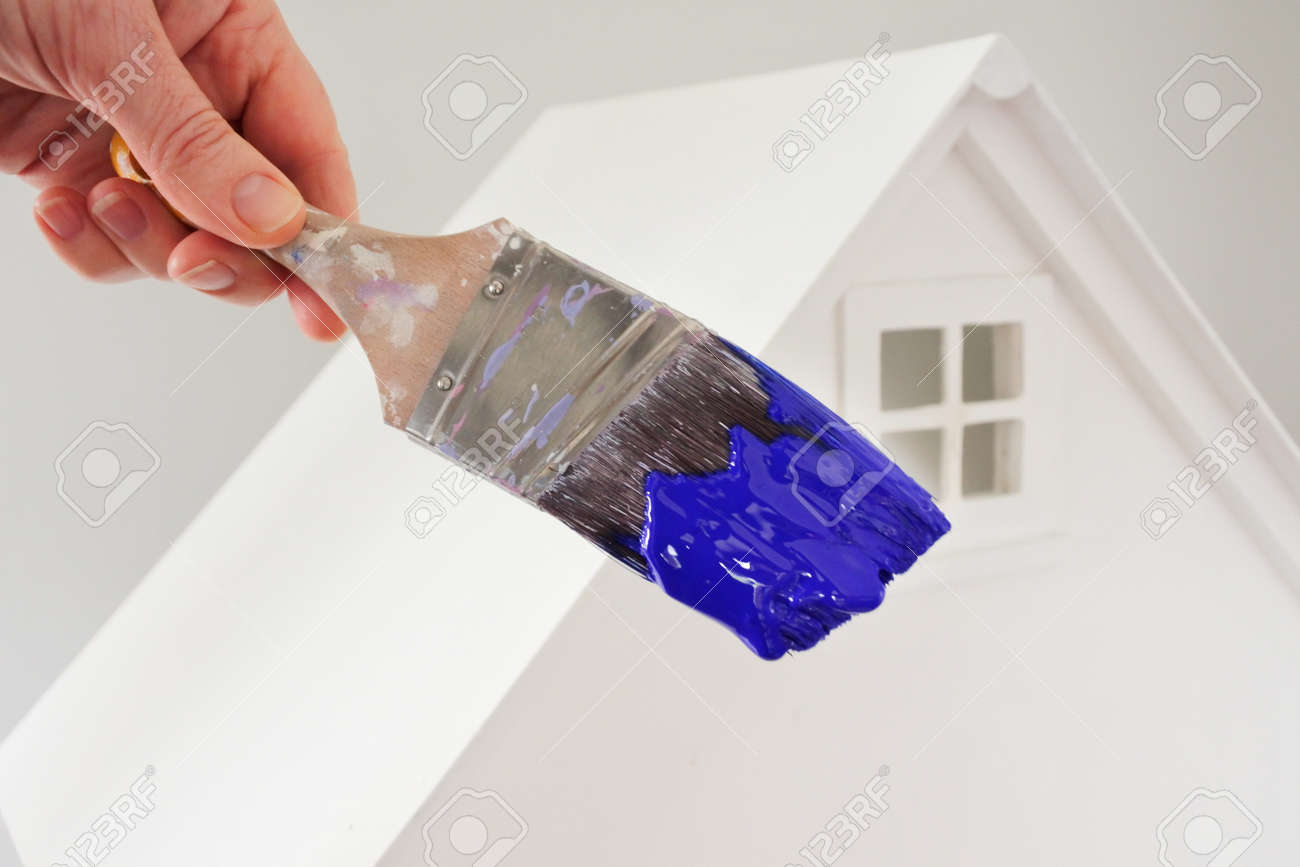 Person holding a paint brush with blue paint color against a white house. Renovation, home decoration and painting house concept. No people. Copy space - 169904660 Person holding a paint brush with blue paint color against a white house. Renovation, home decoration and painting house concept. No people. Copy space - 169904660