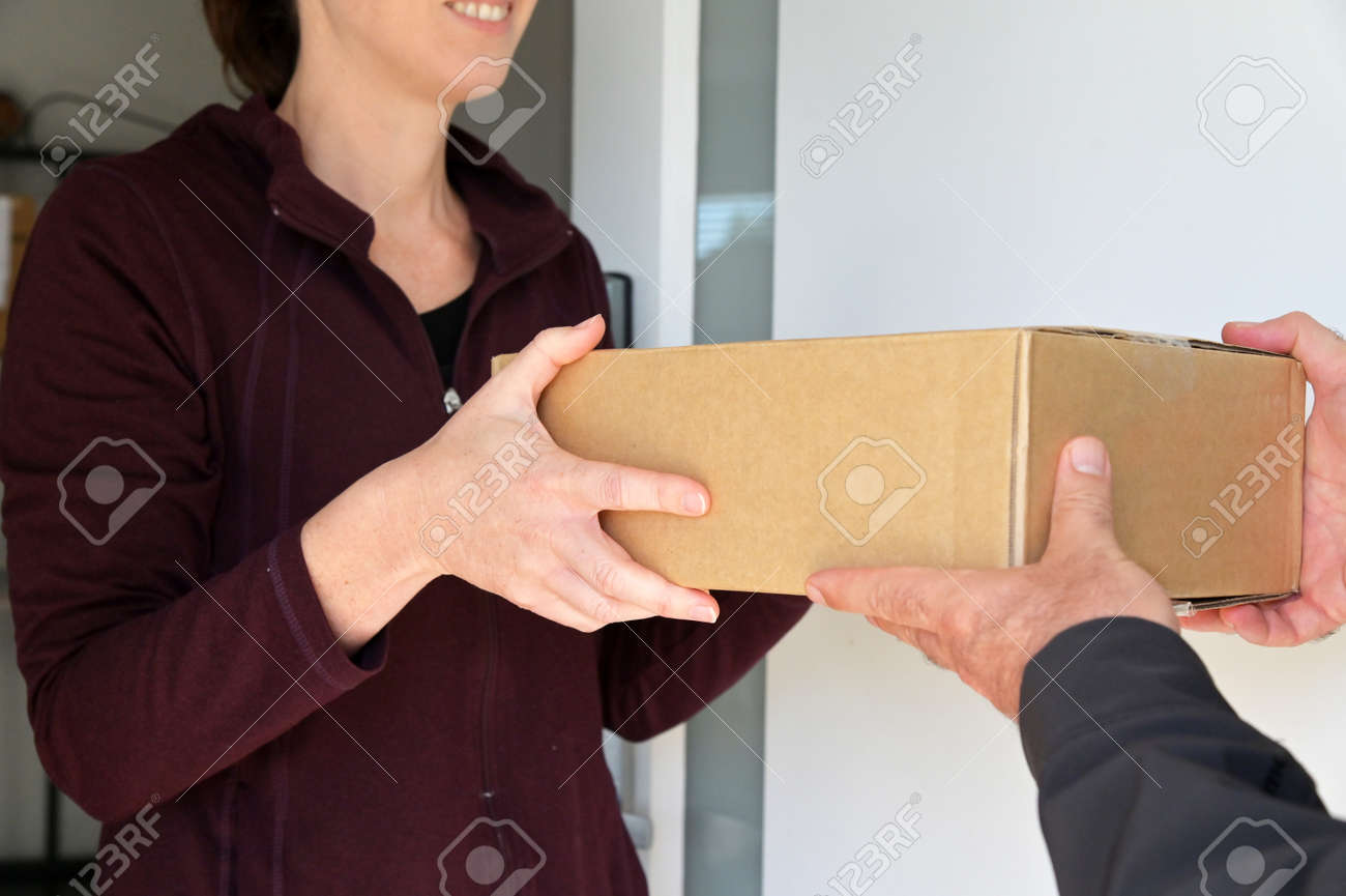 Woman receiving a package from a currier at home front door. - 169904669 Woman receiving a package from a currier at home front door. - 169904669