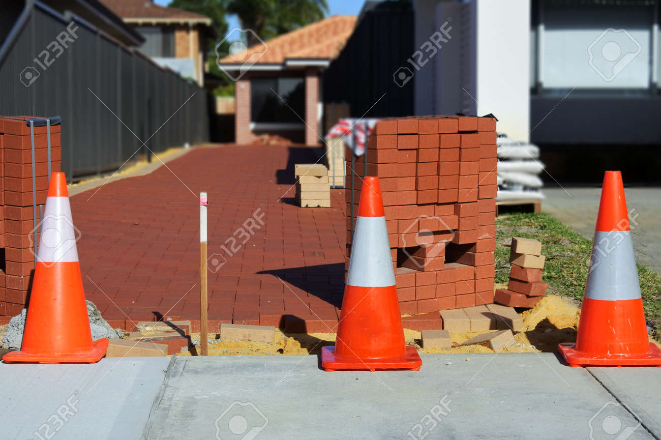 Line of a traffic safety warning cones in front of a new paved driveway with red bricks. . - 169904772 Line of a traffic safety warning cones in front of a new paved driveway with red bricks. . - 169904772