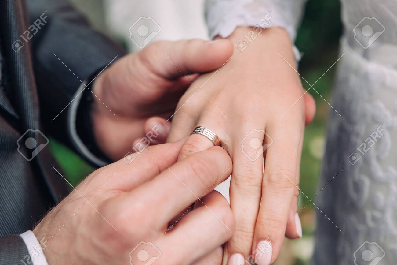 Closeup of the hand of the groom puts a wedding ring on the brides finger, the ceremony on the street, selective focus - 128340571 Closeup of the hand of the groom puts a wedding ring on the brides finger, the ceremony on the street, selective focus - 128340571