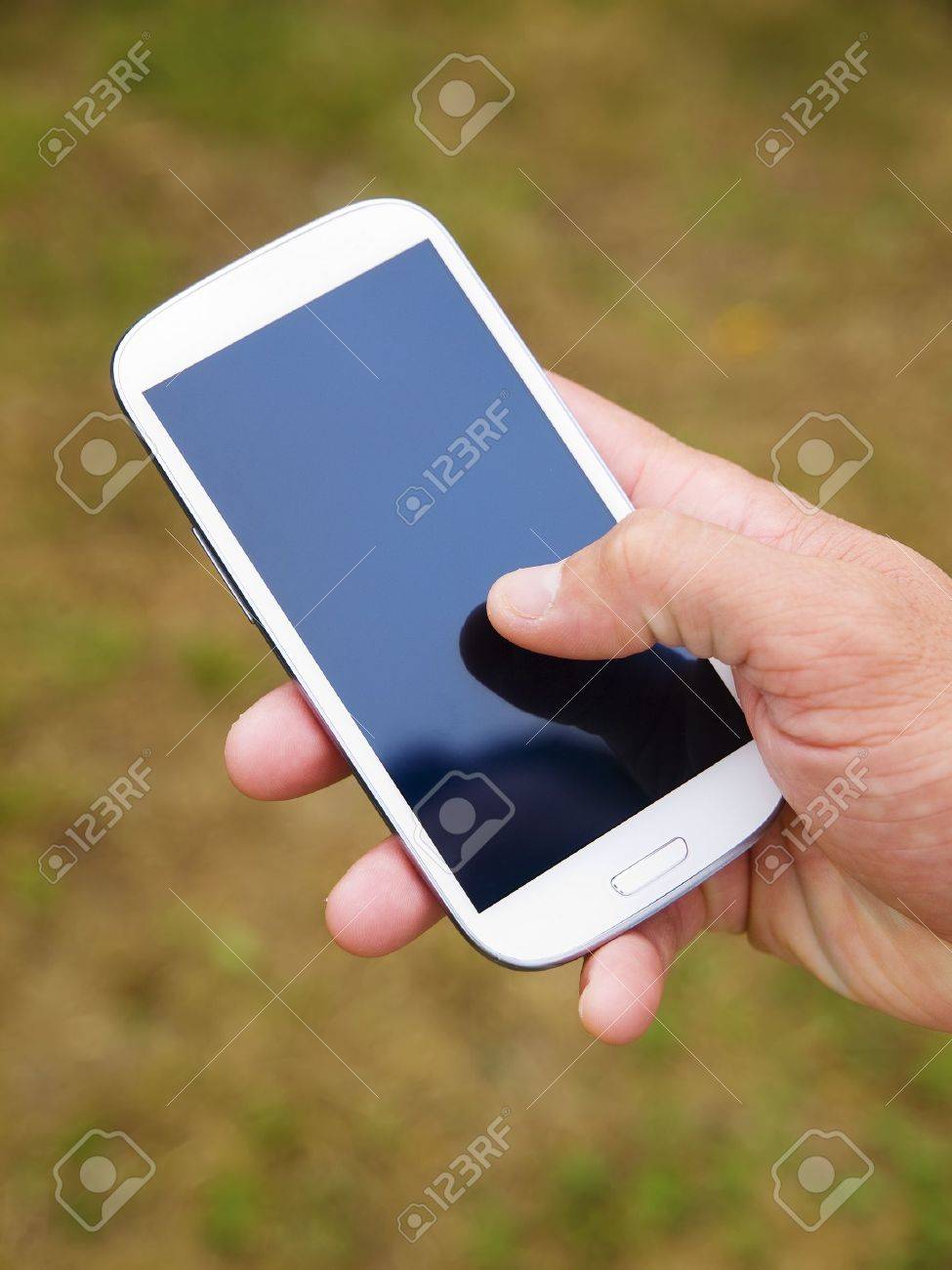 Man hand touching screen on modern mobile smart phone on natural green background - 15224073 Man hand touching screen on modern mobile smart phone on natural green background - 15224073