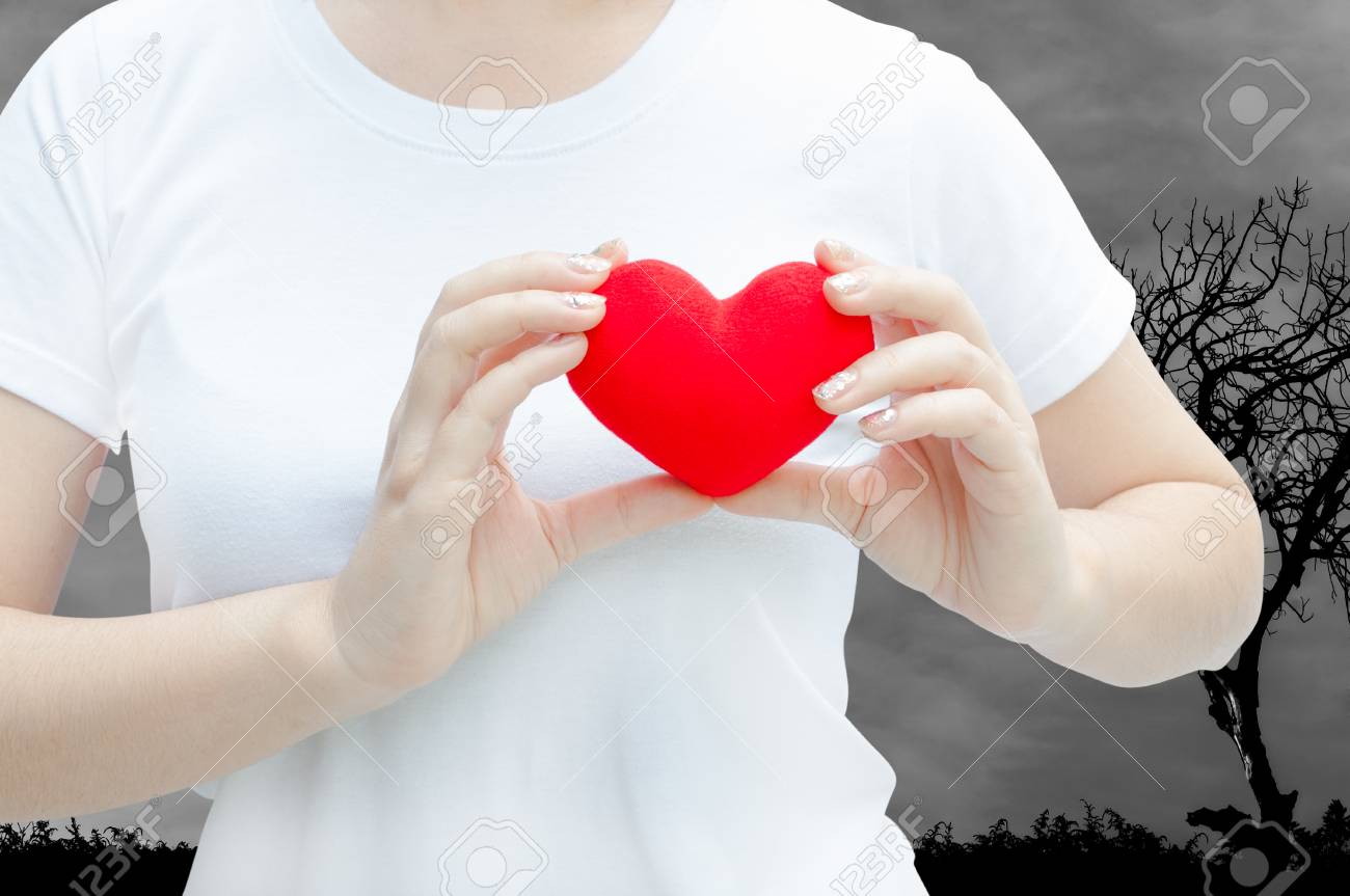 女性の手は自然の暗い背景に彼女の胸を残して赤い心を押さえて手を握る バレンタインデーの概念 愛の心 保護とヘルスケア の写真素材 画像素材 Image