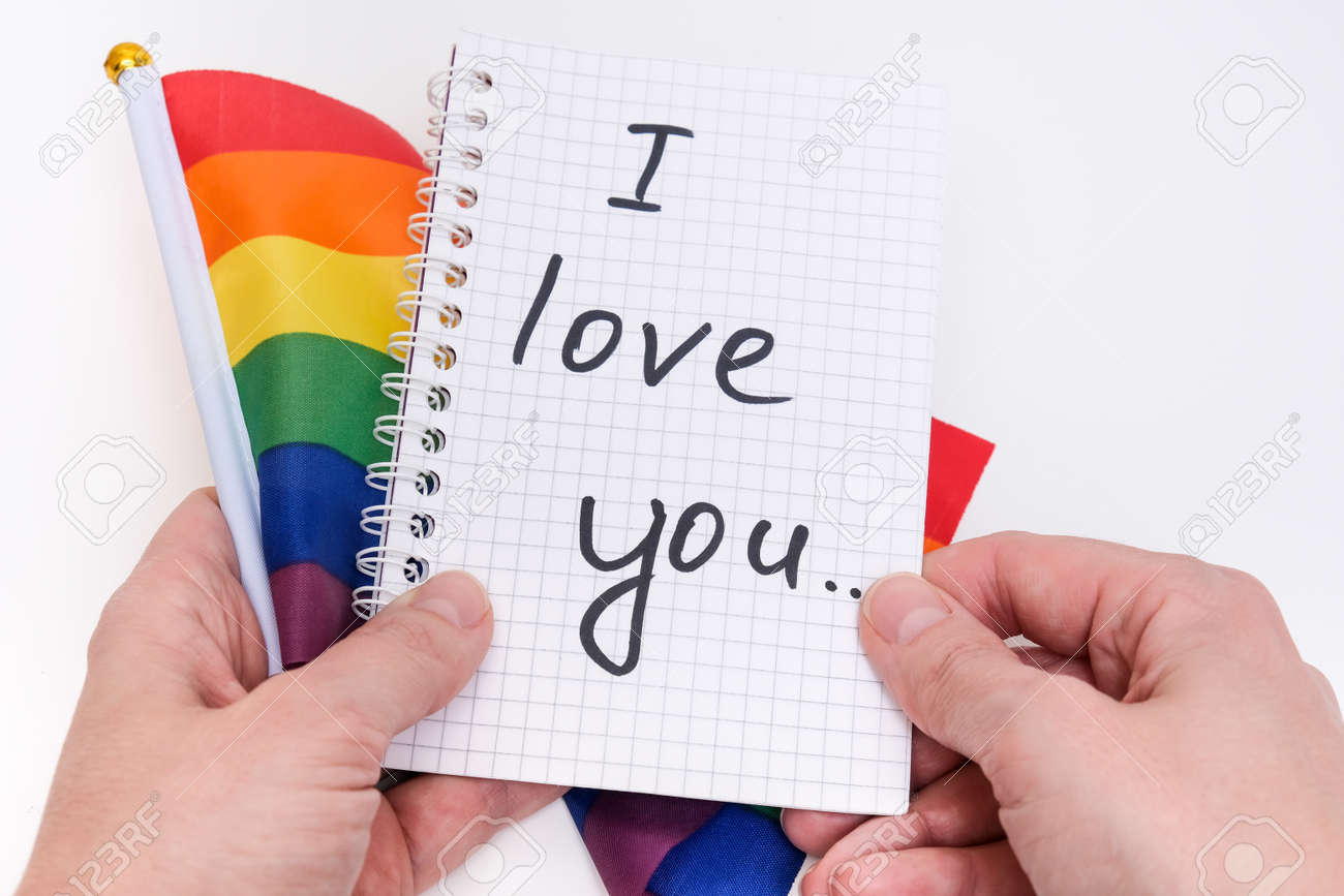 Hands holding a notebook with I Love You inscription and lgbtq rainbow flag on white background - 168193293 Hands holding a notebook with I Love You inscription and lgbtq rainbow flag on white background - 168193293