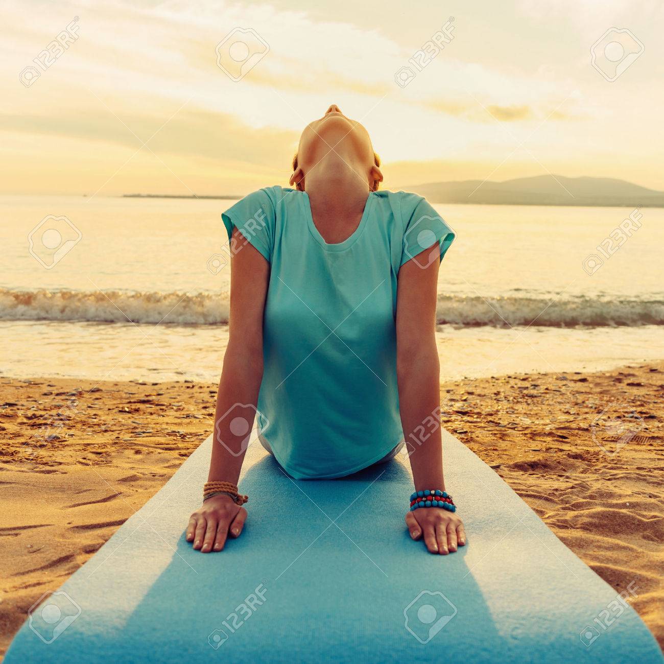 Young woman practicing yoga in upward facing dog pose on beach near the sea on sunset, front view - 49153962 Young woman practicing yoga in upward facing dog pose on beach near the sea on sunset, front view - 49153962