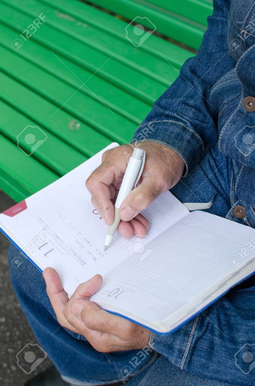 aged man is making notes in the daily planner in the park making a daily planner