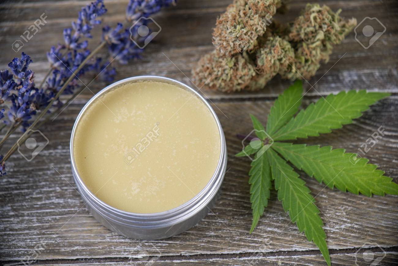 Cannabis hemp cream with marijuana leaf, lavender and nugs over wood background - cannabis topicals concept - 117903359 Cannabis hemp cream with marijuana leaf, lavender and nugs over wood background - cannabis topicals concept - 117903359